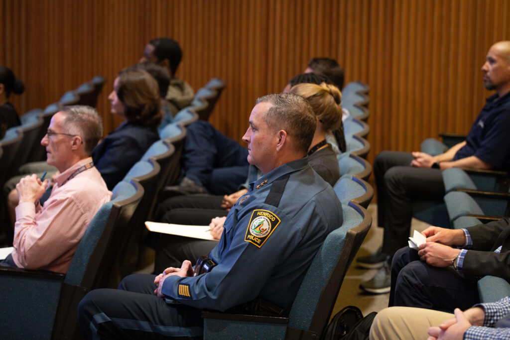 Left profile of three rows of employees watching from the right side of the room, focusing on a Police's Executive Chief, Ken Burnett