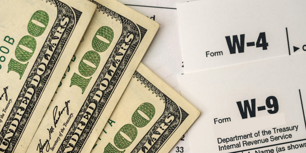 zoomed in photo of hundred dollar bills laying on top of W-4 and W-9 forms